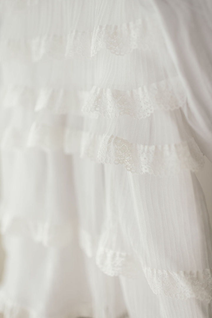 A close-up view of a delicate, white lace dress with multiple layers of ruffled fabric.