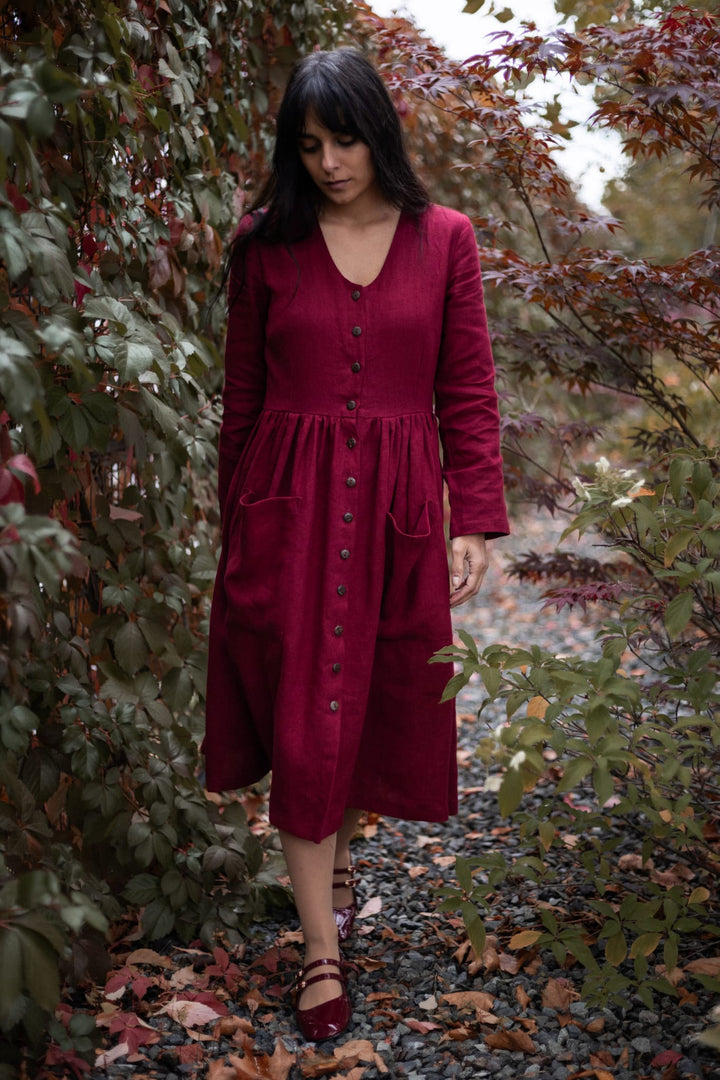 A woman in a red dress walks through a garden with autumn foliage.