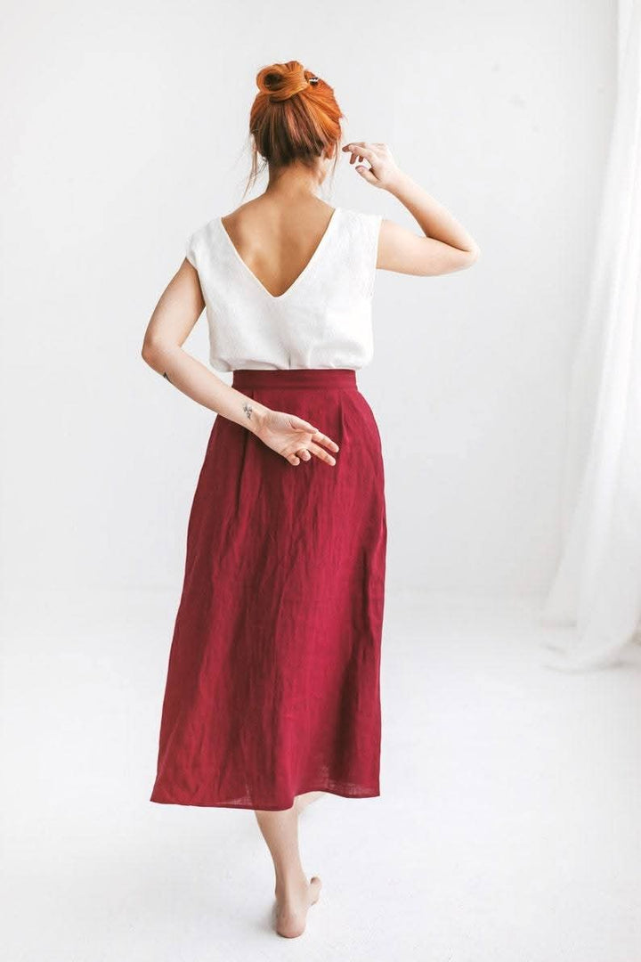 A woman with red hair wearing a white top and a red skirt is standing against a white background.