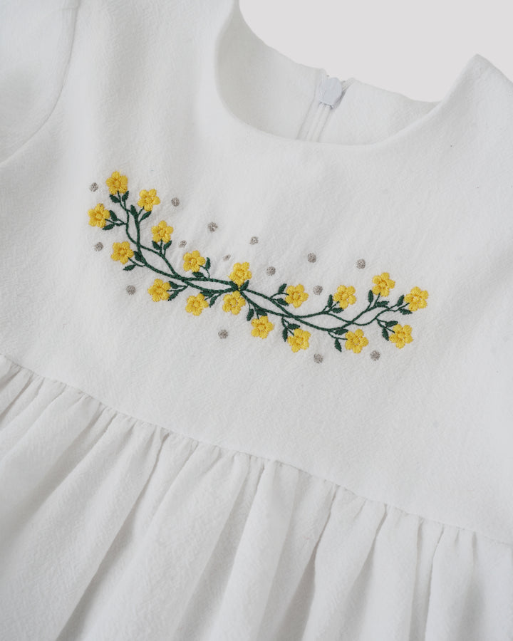 A close-up view of a white dress with a floral embroidered design on the front.