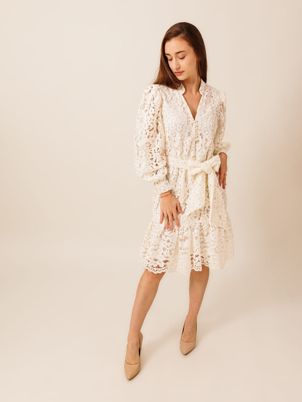 A young woman wearing a white lace dress with a high collar and long sleeves, posing against a plain background.