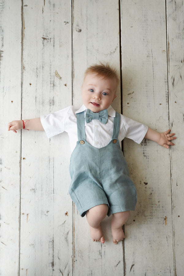 a baby wearing a bow tie and overalls laying on a wooden floor
