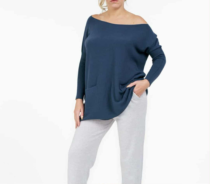 A woman wearing a navy blue sweater and white pants stands against a white background.