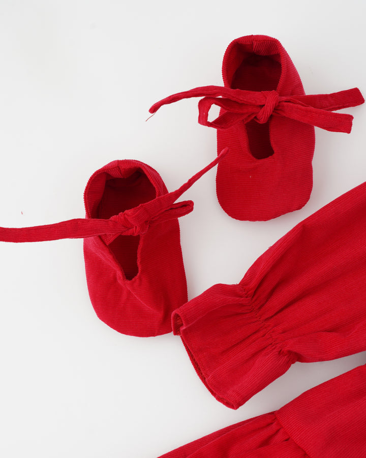 A pair of red baby shoes with bows on a white background.