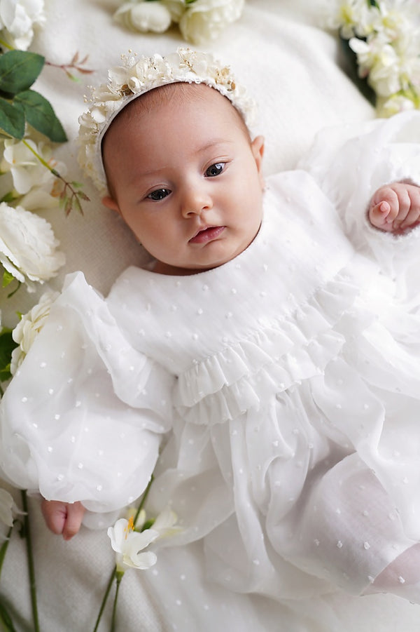 a baby girl in a white dress laying on a bed of flowers