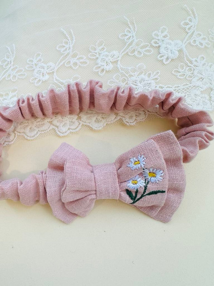 A pink bow tie with white flowers embroidered on it, resting on a white lace background.