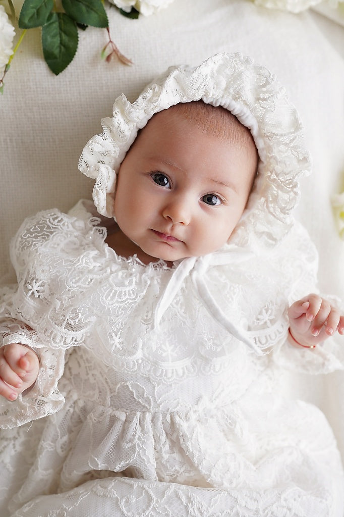 a baby wearing a white dress and bonnet