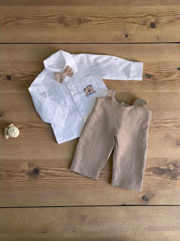 A white shirt with a bow tie and beige pants are laid out on a wooden surface.