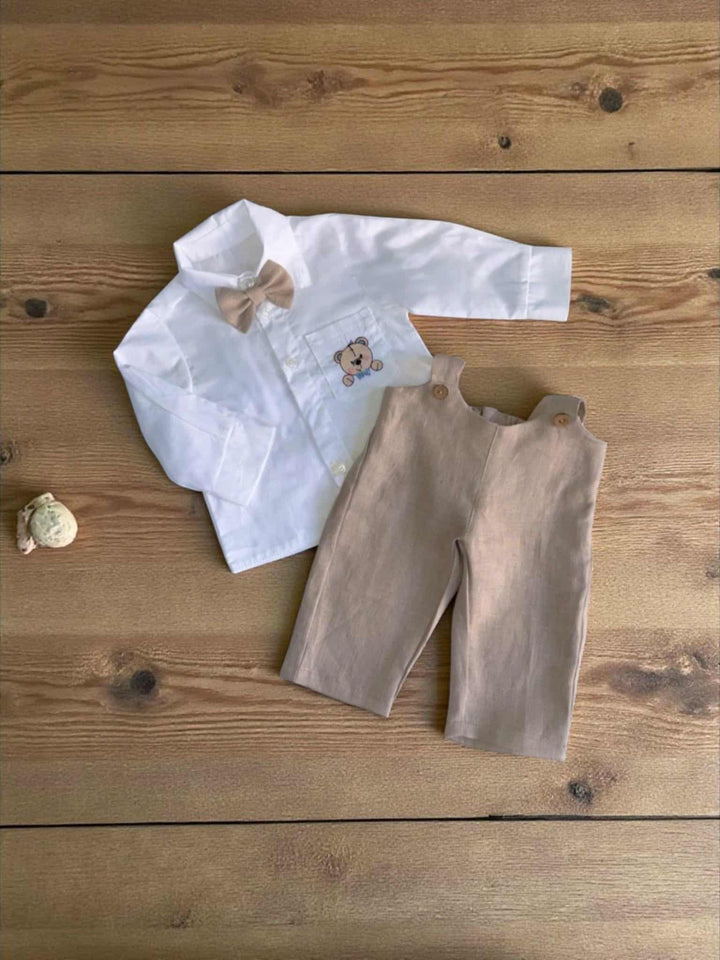 A white shirt with a bow tie and beige pants are laid out on a wooden surface.