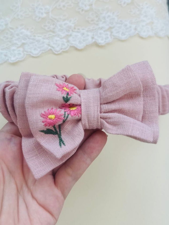 A hand holding a pink bow with a floral embroidered design.