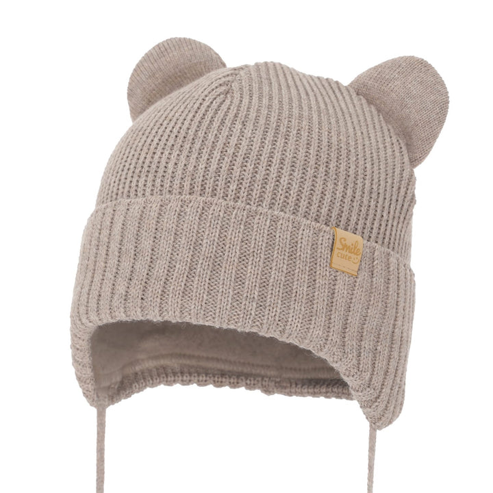 A beige knit hat with pom-pom ears and a yellow tag on the front.