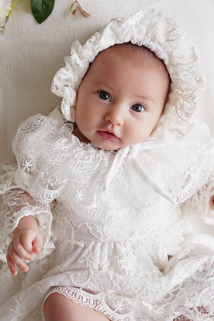 a baby wearing a white dress and bonnet