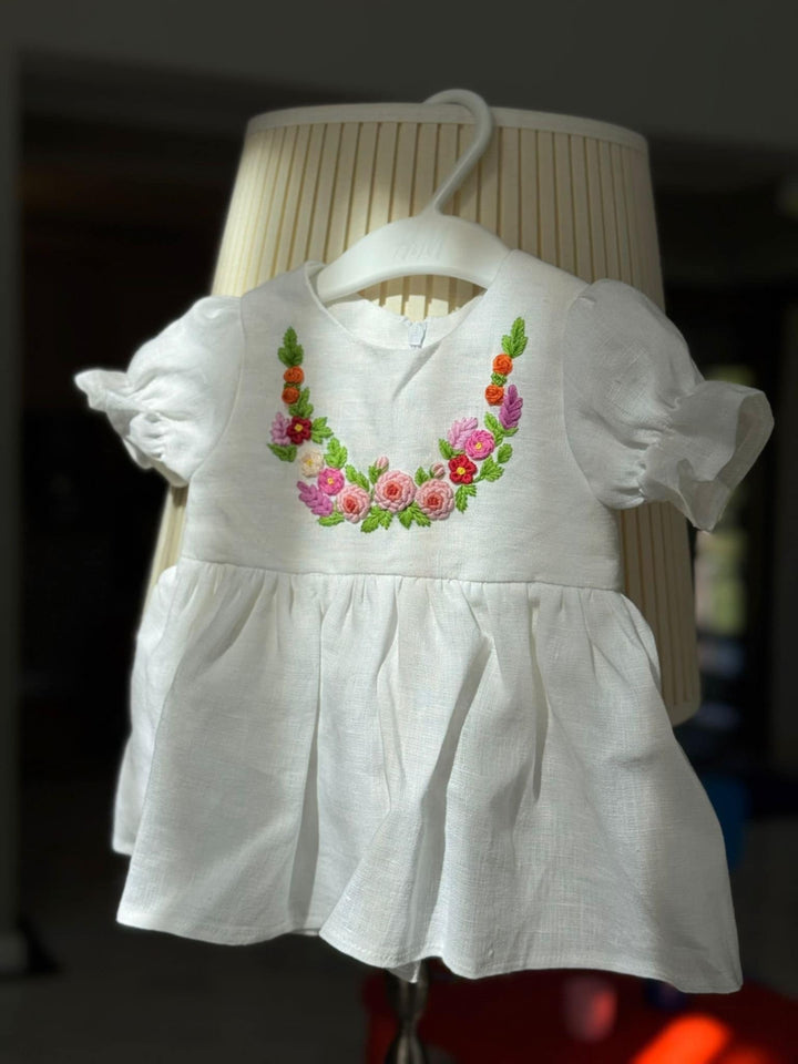 A white dress with a floral embroidered design on the front, hanging on a white hanger.