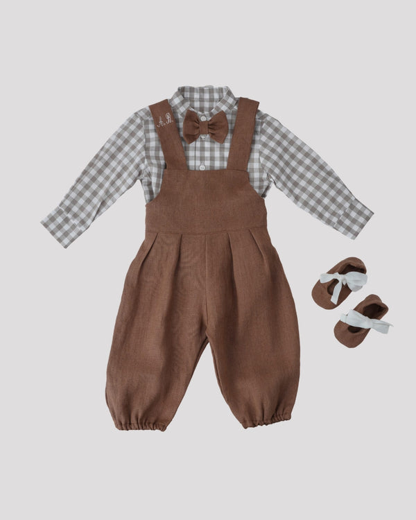 A set of children's clothing consisting of a plaid shirt, brown overalls, and a bow tie, along with a pair of brown shoes.