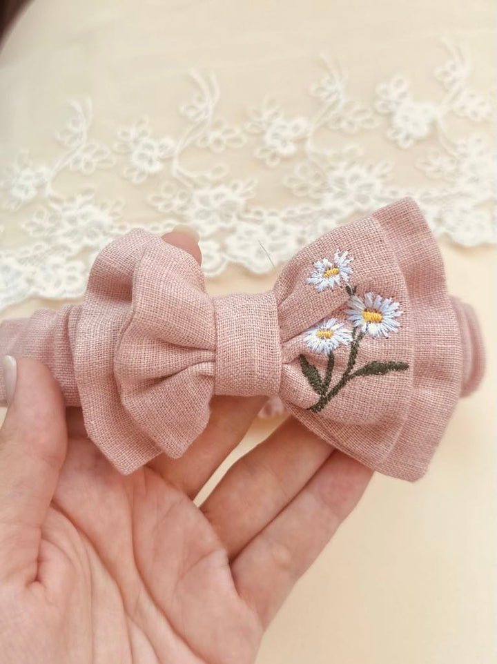 A hand holding a pink bow with white daisies embroidered on it.