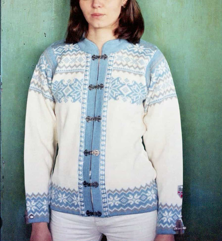 A woman wearing a blue and white patterned sweater stands against a green wall.