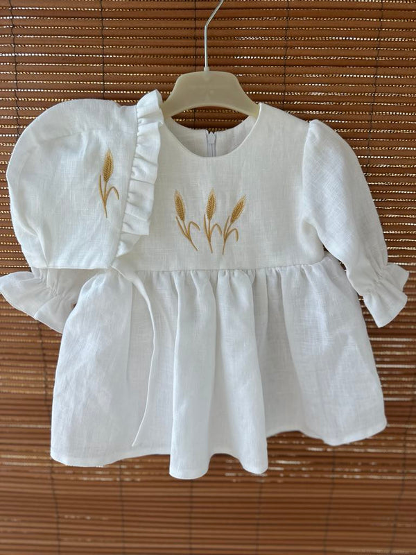 A white dress with gold embroidered designs, including three golden wheat ears, is hanging on a wooden hanger.