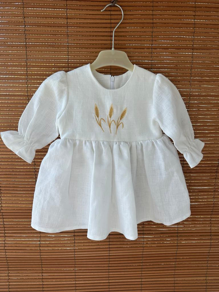A white dress with a ruffled collar and puffed sleeves, featuring a gold embroidered design of wheat stalks on the front.