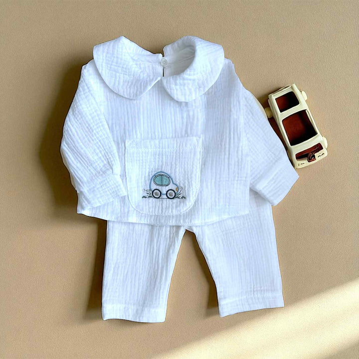 A white outfit with a small car embroidered on the front, placed next to a small toy car on a beige surface.