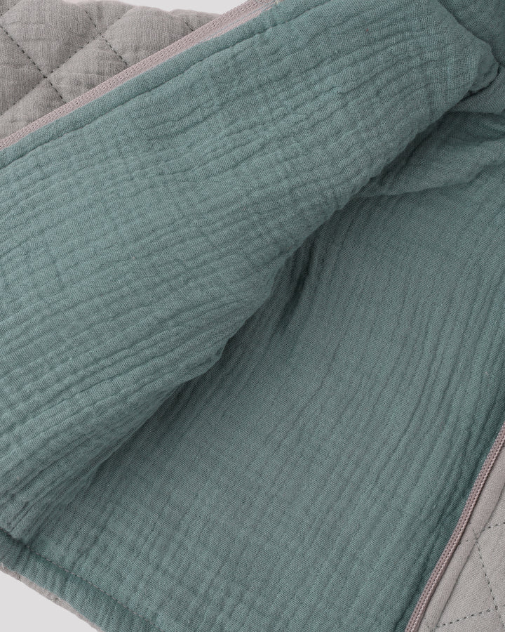 a close-up view of a fabric with a textured, quilted appearance. The fabric appears to be a light green or mint-colored material, possibly a blanket or quilt. The image does not contain any text or other objects, and the focus is solely on the fabric's texture and color.