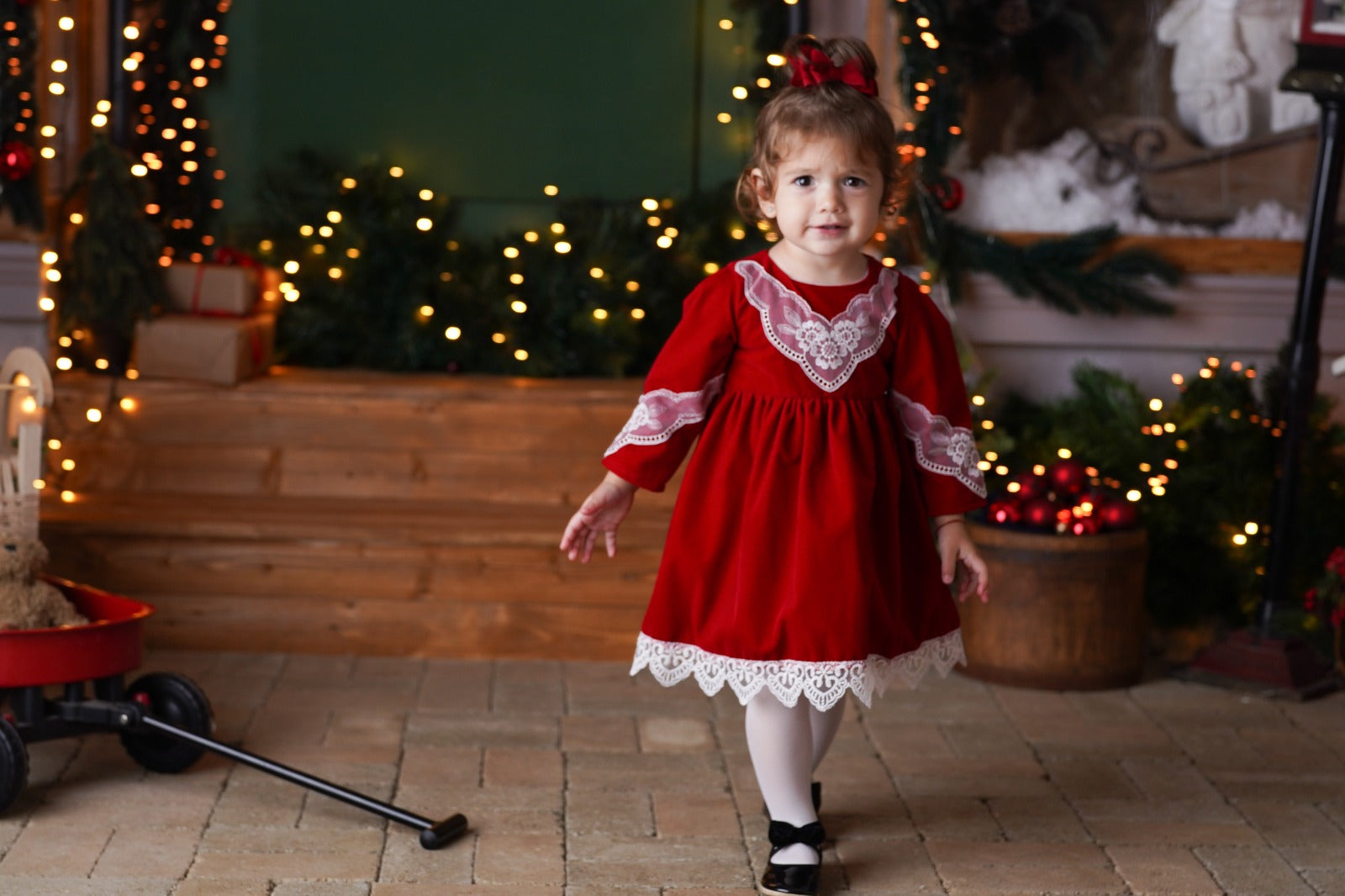 a little girl in a red dress standing in front of a christmas tree