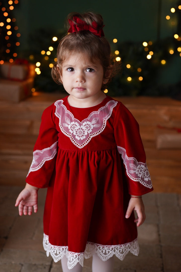 a little girl wearing a red dress and white tights