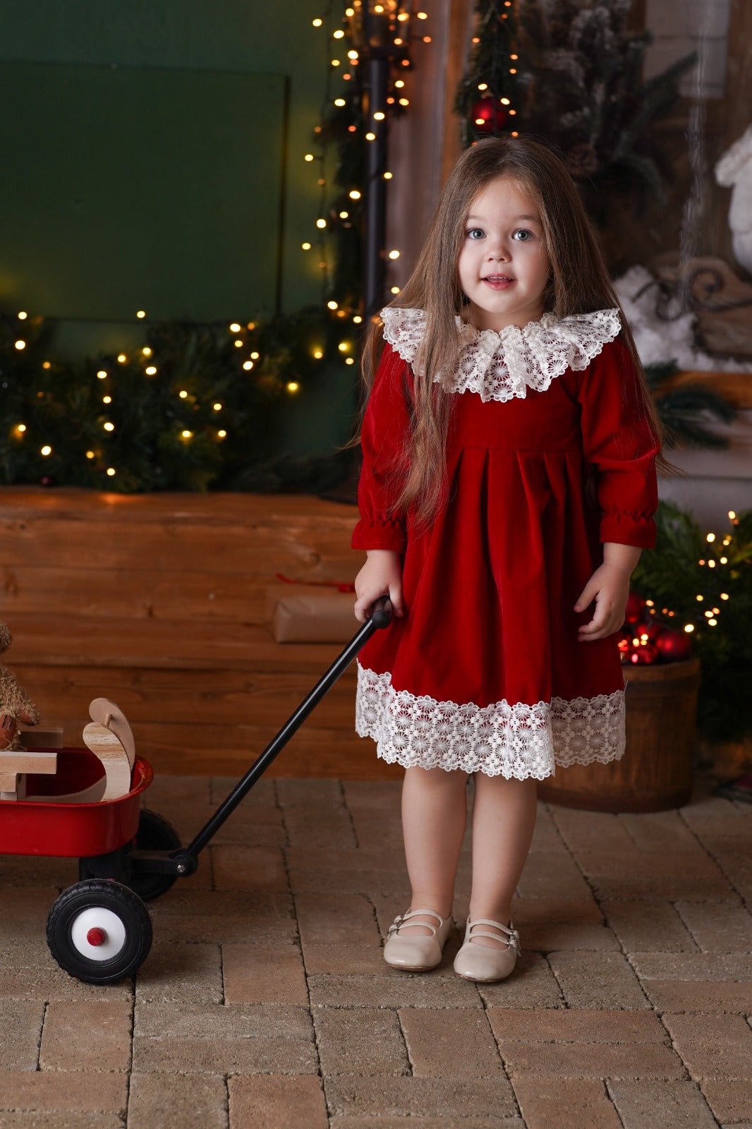a little girl in a red dress is pulling a red wagon